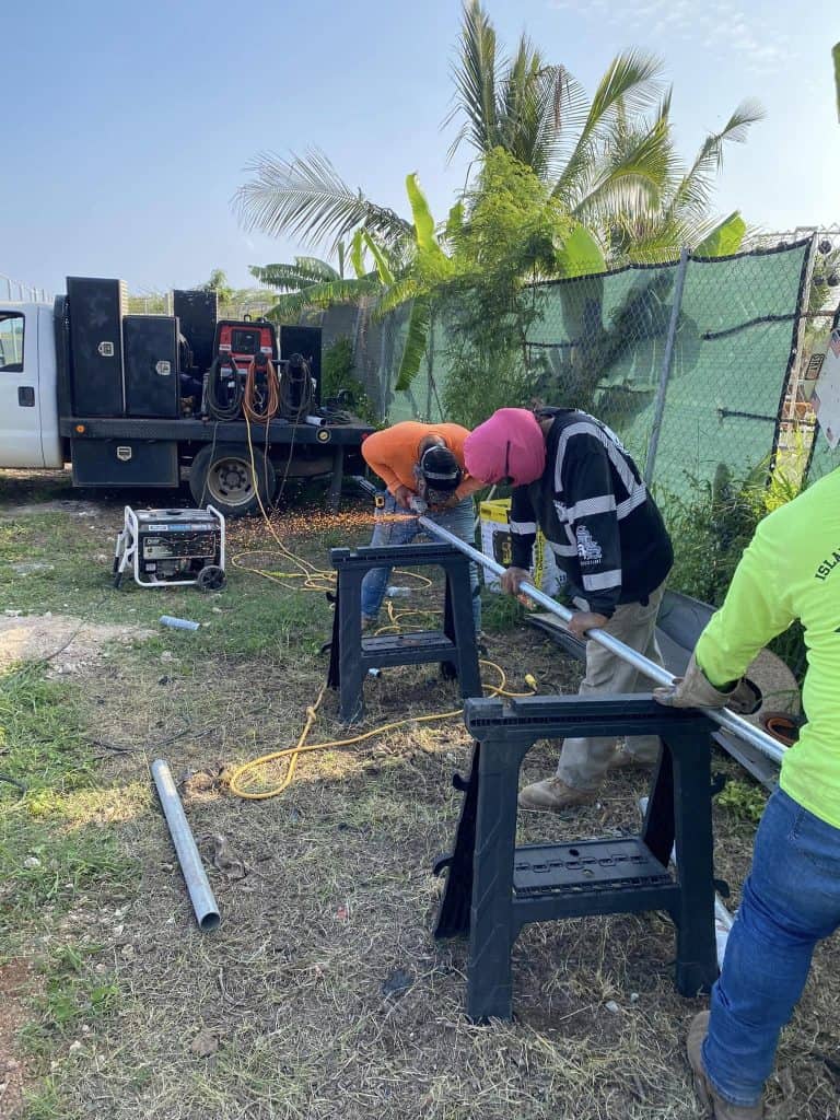 Workers cutting metal fence posts during chain-link fence installation in Kapolei.
