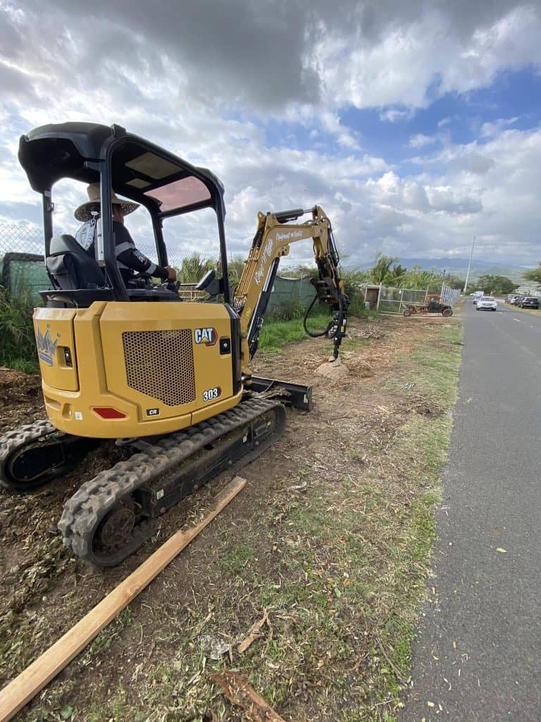 Excavator drilling post holes for a new chain-link fence installation in Kapolei.