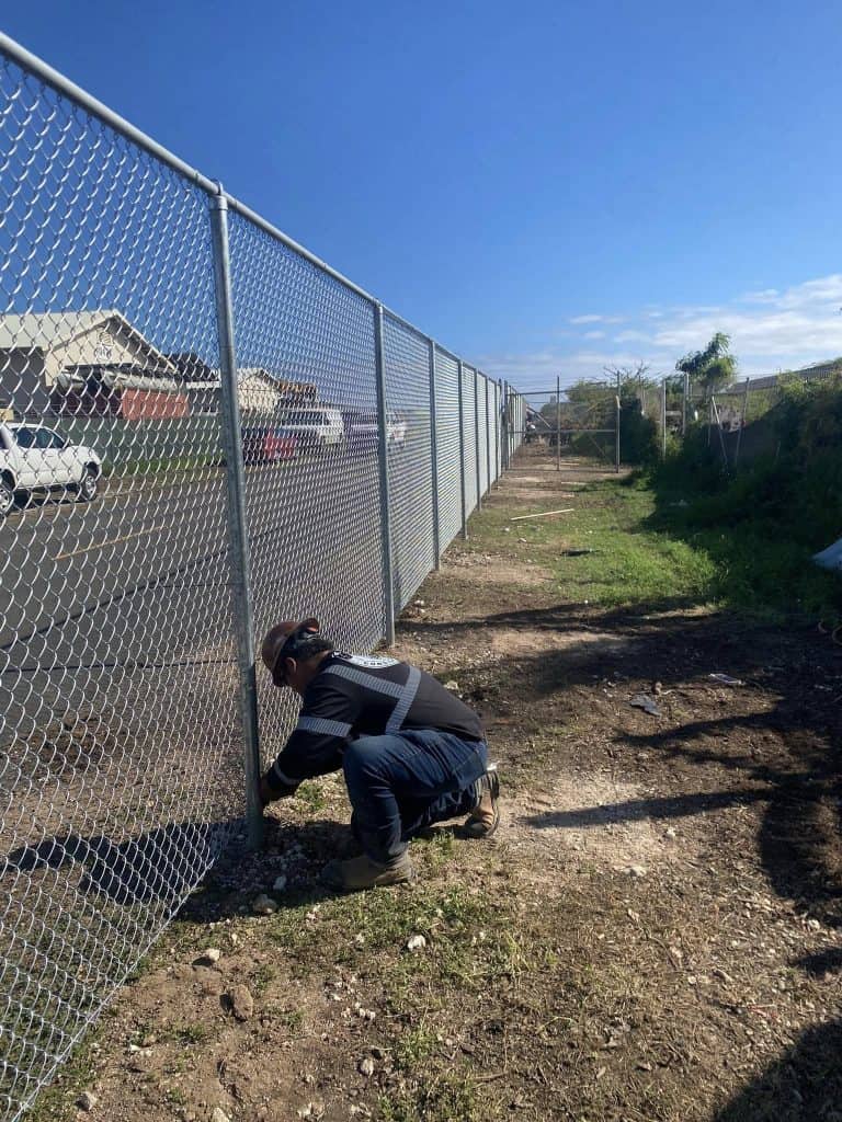 Worker fastening chain-link mesh to fence posts during installation in Kapolei.