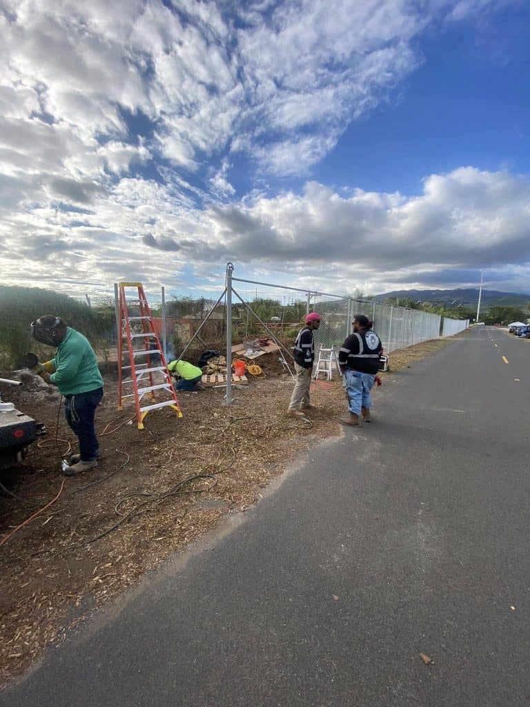 Crew installing and leveling the corner post for a chain-link fence in Kapolei.