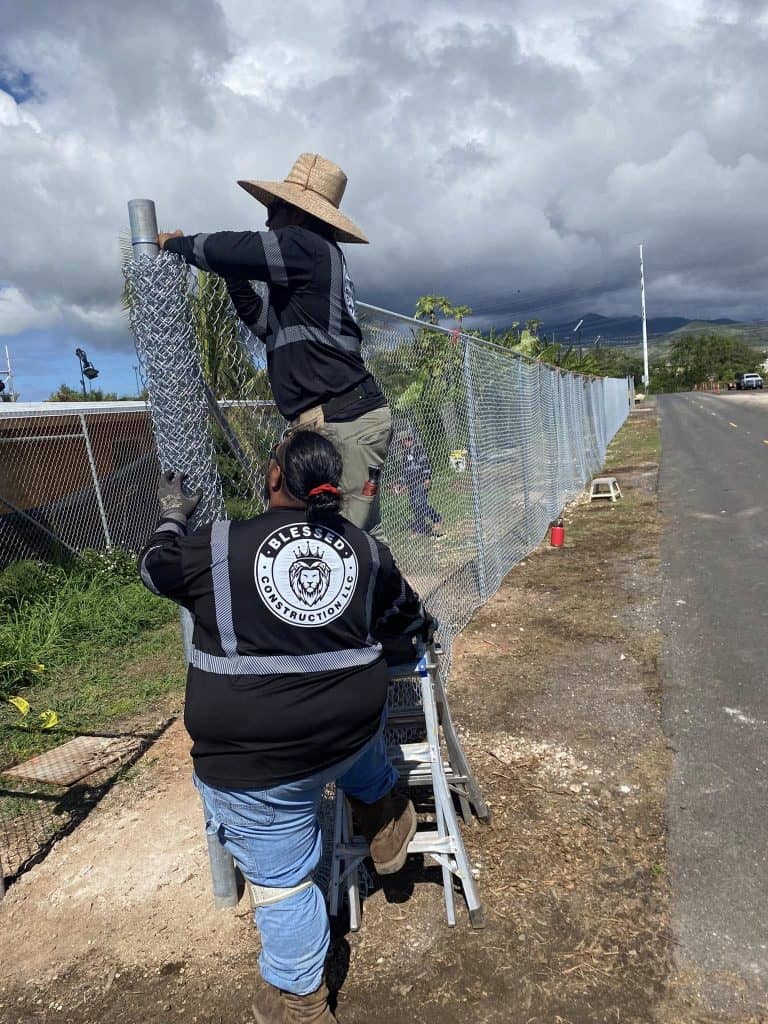 Crew stretching and securing chain-link fencing to posts in Kapolei.