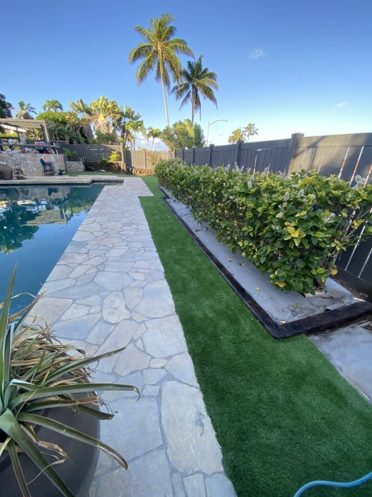 Artificial turf installation beside pool deck with clean stone walkway and hedge in Kapolei.