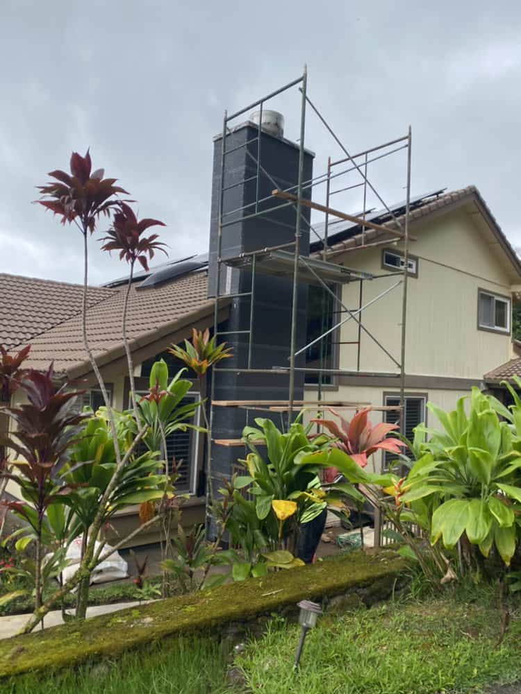 Completed rock veneer chimney with scaffolding removed and Koʻolau mountains in the background