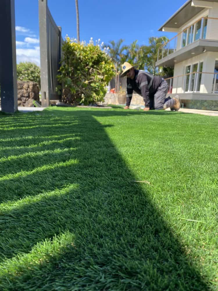 Installer shaping and securing artificial turf during a backyard installation project.