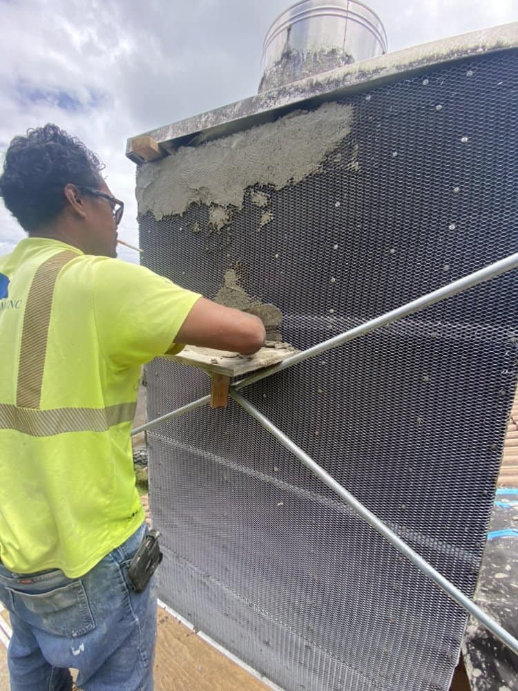 Applying the base scratch coat over the metal lath during the chimney rebuild