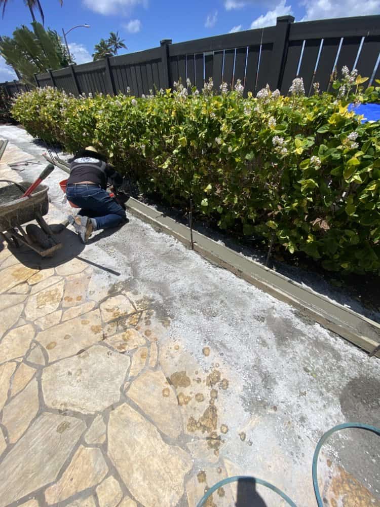 Workers installing stamped concrete borders along the edge of the turf area.