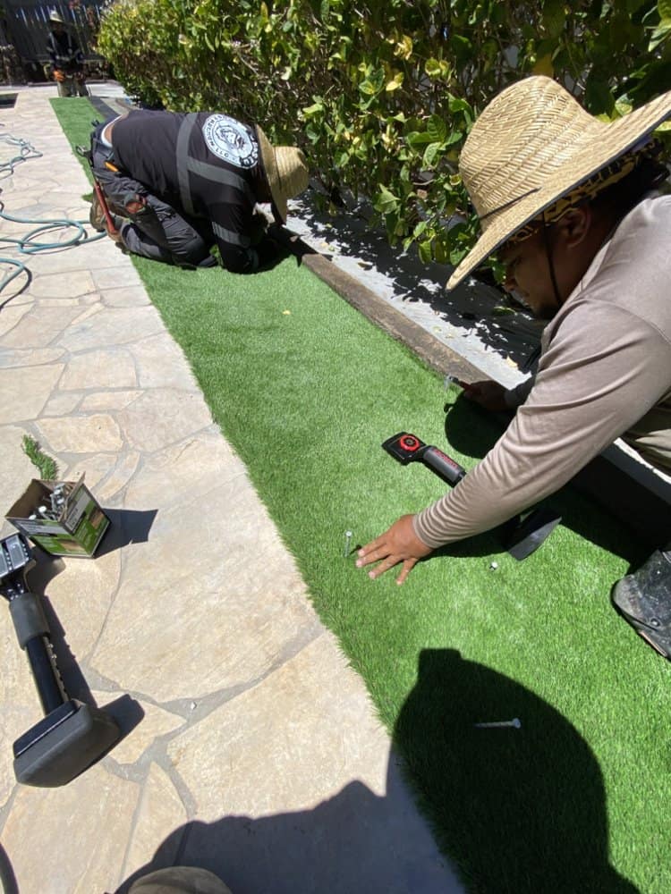 Crew cutting and fitting artificial turf along the stone walkway.