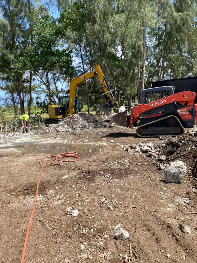 Alt text: Excavator and compact track loader clearing demolished concrete debris.