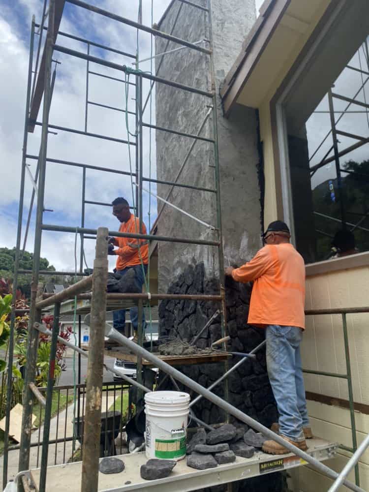 Craftsman installing individual blue rock pieces onto the chimney face