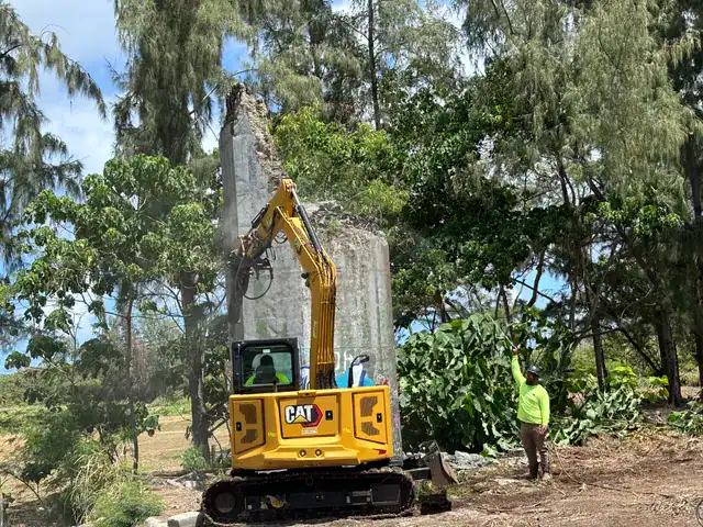 Excavator pulling down and removing tall concrete pillars during demolition.