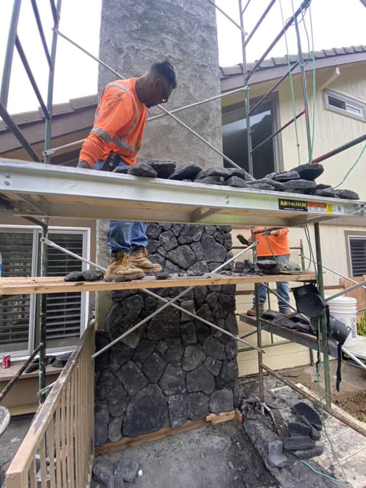 Wide scaffold view showing workers installing blue rock veneer on the chimney