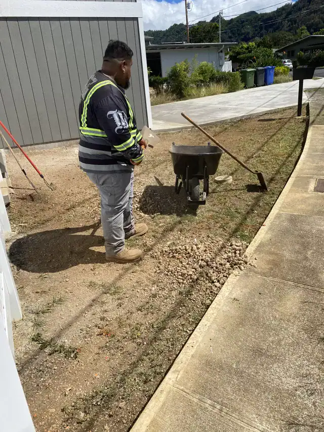 Worker grading and leveling soil during paver installation in oahu