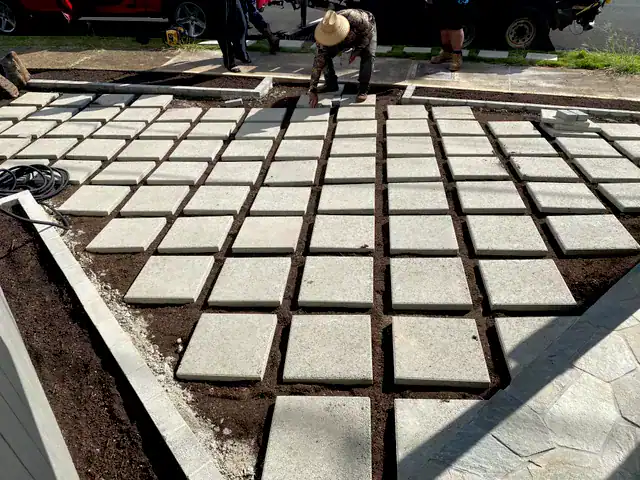 Grid-style concrete pavers being laid in place during installation